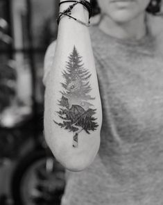 a woman with a bear and pine tree tattoo on her arm