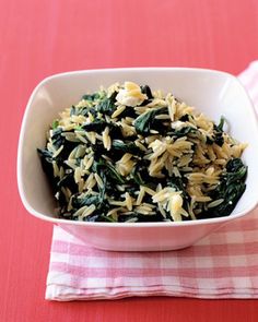 a white bowl filled with pasta and spinach on top of a red table cloth