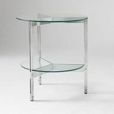 a glass table with metal legs and a shelf on one side that has a round glass top