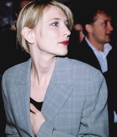 a woman with short hair wearing a suit and red lipstick looking off to the side