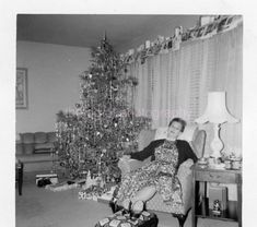 an old black and white photo of a woman sitting in front of a christmas tree