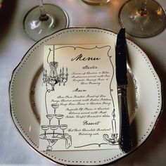 a menu on a plate next to some wine glasses and silverware with a knife