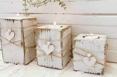 three white boxes with hearts on them are sitting in front of a wall and one has a candle