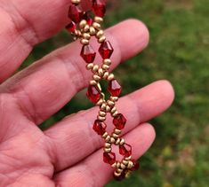 a hand holding a red and gold beaded necklace in it's left hand