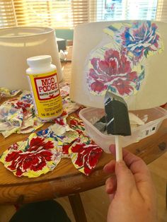 a person is painting flowers on paper with glue and a paintbrush while sitting at a table