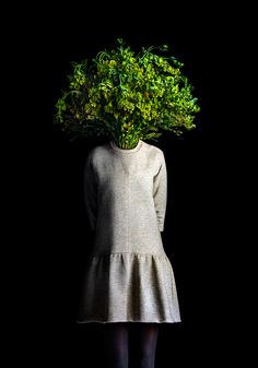 a woman standing in front of a black background with a plant on her head and legs