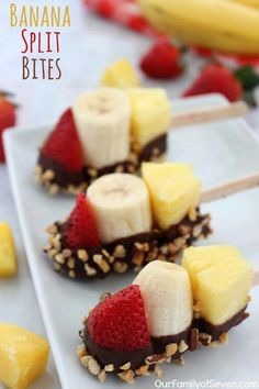 banana split bites with chocolate and strawberries on a white plate next to sliced bananas