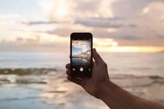 someone holding up their cell phone to take a photo with the ocean in the background