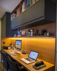 two laptops are sitting on a desk in front of a bookshelf and shelves