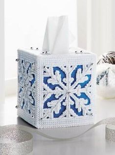 a tissue box decorated with blue and white crocheted snowflakes is sitting on a table