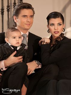 a man in a suit and tie holding a baby while sitting next to a woman