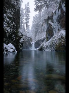 a river surrounded by snow covered rocks and trees in the distance with water running through it