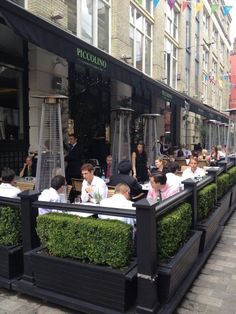 people sitting at tables in front of a restaurant on a city street lined with tall buildings