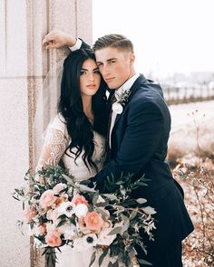 a bride and groom standing next to each other in front of a wall with flowers