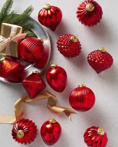 red christmas ornaments on a white table with gold ribbons and bows, including one ornament