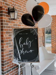 a baby shower sign with balloons hanging from it's back and in front of a brick building