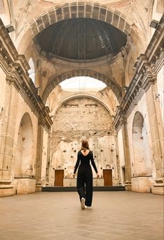 a woman walking through an old building with stone arches and arched doorways on both sides