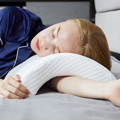 a woman laying on top of a bed with a pillow in her hand and eyes closed