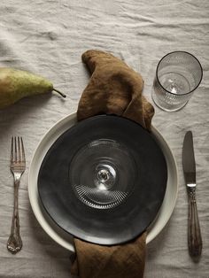 an empty plate and silverware on a white table cloth with a pear next to it