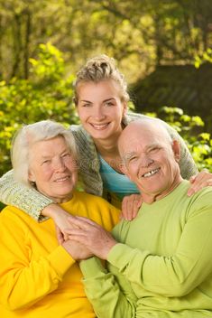 an older couple hugging and smiling for the camera with trees in the background on a sunny day