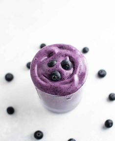 a blueberry smoothie in a cup on a white surface surrounded by blueberries