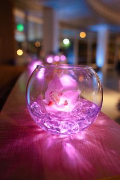 a fish bowl filled with pink flowers sitting on top of a table