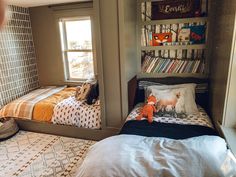 two beds in a small room with bookshelves on the wall and pillows on the floor