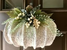 a white pumpkin decorated with greenery and berries hanging from the front door for fall