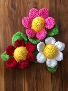 three crocheted flowers sitting on top of a wooden table