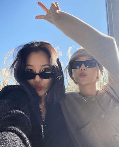 two women pose for the camera with their hands in the air and one is wearing sunglasses