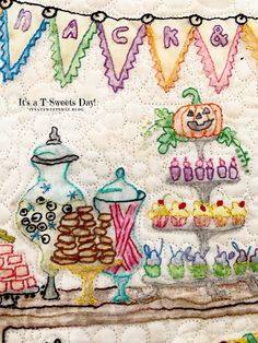 a quilted wall hanging with an assortment of cakes and cupcakes on it