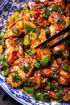 a blue and white plate topped with chicken, peppers and sauce next to chopsticks