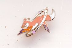 a pink and white brooch with an orange fox on it's back side