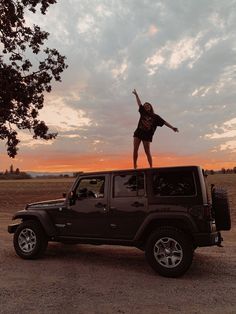 a woman standing on top of a black jeep in the middle of a dirt field