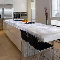 a kitchen with an island, stove and refrigerator freezer next to two black chairs