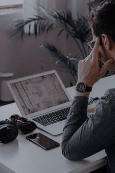 a man sitting in front of a laptop computer on top of a white desk next to headphones