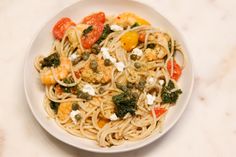 a plate of pasta with shrimp, tomatoes and fettuccine on a marble table