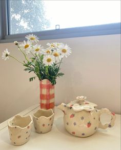 a vase with daisies in it sitting on a table next to two teapots