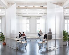 four people sitting on benches in the middle of an open room with white walls and windows