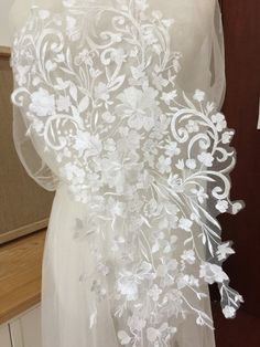 the back of a wedding dress with white flowers on it and a veil draped over it