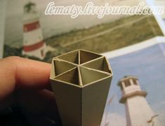 a hand holding an origami object with a lighthouse in the backgroun