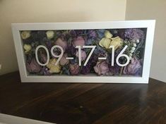 a white frame with flowers and the number nine on it is sitting on top of a wooden table