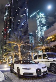 two bugatti cars parked in front of a tall building at night with palm trees