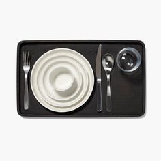 a place setting with silverware and utensils on a black tray against a white background