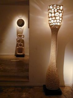 a tall lamp sitting on top of a wooden floor next to a white vase with holes in it