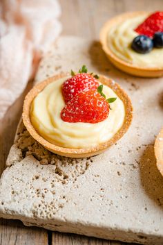 three small desserts with strawberries and blueberries in them on a stone slab