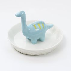 a small blue toy dinosaur sitting on top of a white plate with a yellow stripe