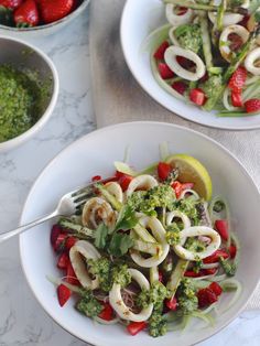 two white bowls filled with pasta and veggies on top of a marble table