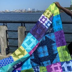 a person holding up a colorful quilt by the water