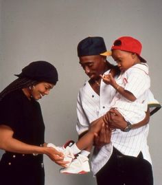 a man holding a baby while standing next to two women and a young child in front of a white wall